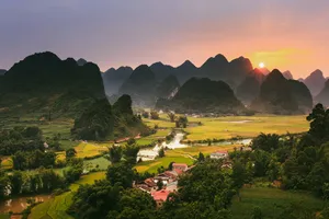 Cao Bang karst mountains at sunrise above terraced fields and a riverside village during the 3D3N motorbike loop