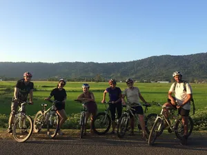 Cyclists with helmets and bicycles paused on a country road through fields and hills in Langkawi on a guided tour