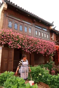 Pink flowering vines spilling over a Naxi-style wooden building in Lijiang Old Town, a traveller pausing in the garden