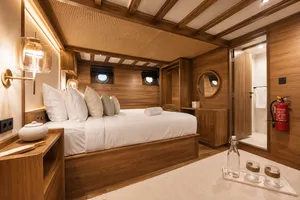 Travass Life new phinisi suite with neatly made beds, warm wood finishes, porthole windows and a fire extinguisher for Komodo Island