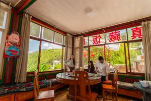 Lodge dining room in Shangri-La with large windows to green hills, travellers at a round table preparing snacks
