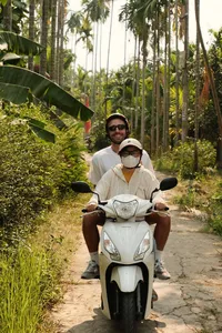 Helmeted motorbike riders smiling on a quiet path through palm trees in Hoi An during the early-morning trades tour