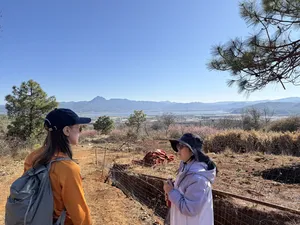 Travellers stop on a rural viewpoint above Lijiang, looking over dry fields and distant mountains during a Yi & Naxi trek