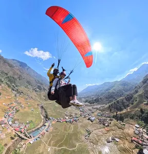 Two paragliders floating over patchwork terraces and a winding river, red-orange canopy catching the wind above the mountains in Sapa