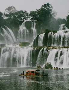 Cascading waterfall in Cao Bang with a small boat floating on the river below, Ha Giang Expeditions motorbike tour