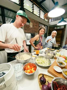 Shared cooking session at Kebun Lidstari farmhouse kitchen in Langkawi, with people chopping vegetables and stirring pots during prep