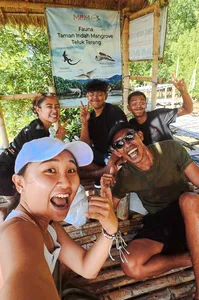 Smiling visitors posing at a mangrove village jetty with a banner for Taman Indah Mangrove during a day trip in Labuan Bajo