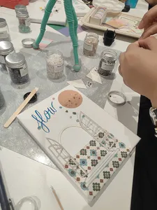 Hands arranging a gemstone vision board at Gemstory in Singapore, surrounded by jars, brushes, and paper crafting materials
