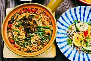 Steaming Yunnan-style noodle broth with greens and red chillies in a terracotta pot, plus a lemony side salad in Lijiang