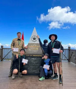 Trekkers posing at the Fansipan âTop of Indochinaâ sign on a 1-day eco trek in Sapa, with clouds above the summit
