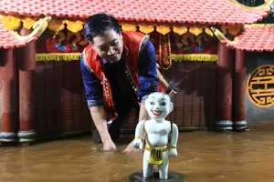 一只迷你的白色水上木偶立在舞台地面上,操偶师正把它摆放在河内装饰精美的剧场里