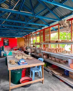 Pottery workshop at Ilham Ceramic in Langkawi with rows of terracotta ceramics on shelves and workbenches under a blue roof.