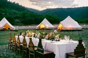 Shangri-La mountain valley camp dinner with set dining table in front of lit white tents at dusk, Mission Liotard stay