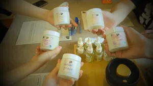 Hands raised holding labelled coco-soy candle jars over a table of oils and wicks during a Singapore candle workshop