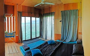 Sea lodge bedroom in Semporna with a double bed, blue curtains and floor-to-ceiling windows looking out to the ocean