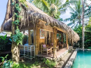 Thatched-roof bamboo cabana beside a turquoise swimming pool surrounded by lush tropical plants at Omunity Bali in Bali