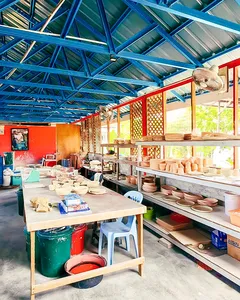 Wide view of Ilham Ceramic Studio in Langkawi, with blue rafters, rows of ceramics on racks, and tools on benches