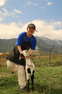 Seeker Yunnan Coffee Estate host in a blue apron holding a black-and-white goat on a mountain coffee farm in Lijiang