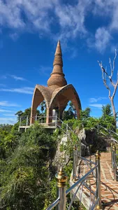 Bronze pagoda tower rising above a garden walkway with metal railings under a blue sky in Khao Sok National Park