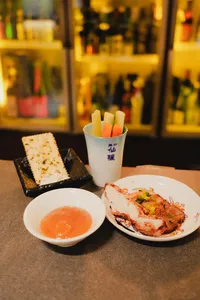 Savoury appetisers and sake tasting cups on a table in a tucked-away Singapore shop, with bottles lining the bar