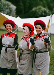Three women in traditional Tibetan-style outfits and red fur hats smiling at a camp in Shangri-La’s remote valleys