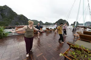 Group stretching on the deck of a Cat Ba boutique cruise, with limestone karst cliffs under an overcast sky at the bay