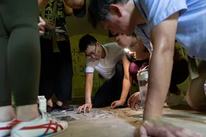 People huddled over a map and cards by lantern light, solving clues during Fort Serapong discovery adventure in Singapore