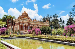 Ornate gold-and-cream temple building in a landscaped garden beside a still pond in Ho Chi Minh City, Vietnam