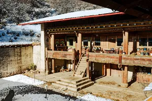 Snow-dusted courtyard and wooden Tibetan-style building with steps and railings at a camp stay in Shangri-La, Ferme Liotard