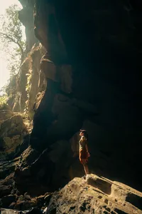 Cave trekker on a rocky ledge inside Phong Nha-Kẻ Bàng cave, looking toward daylight on a Greenland Tours visit