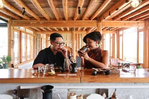 Lijiang coffee workshop with a wooden counter and long windows, two people sipping and tasting brewed coffee