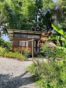 Wood-and-glass cabin at Kebun Lidstari farmstay in Langkawi, tucked into a colourful tropical garden with blooms and banana leaves