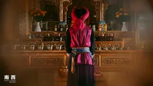 Back view of a person in ceremonial red robes and tall hat facing a shrine of brass bowls at a Khampa Caravan homestay in Shangri-La