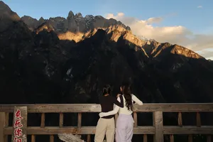 Two hikers at a stone-and-wood lookout, backs to the camera, taking in steep cliffs of Tiger Leaping Gorge near Lijiang on a 2D1N high trail
