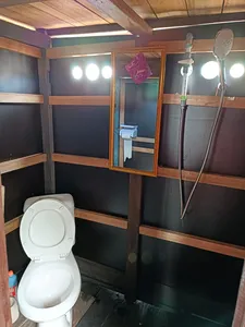 Boat bathroom on board with a white toilet, wall lights, and a mirror inside wooden bunk walls on a 3D2N cruise, Tanjung Puting