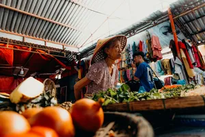 会安一处色彩缤纷的市场摊位前，一位戴着花纹斗笠的本地摊贩正在整理绿叶菜，供家常烹饪用