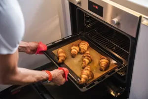 Hands in red oven gloves sliding a tray of croissants out of the oven at French Cooking Lab in Singapore