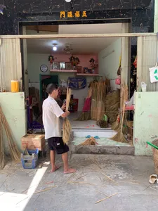 Saigon craft workshop doorway with thatched bundles and floor mats hanging, an artisan holding straw while preparing bundles inside