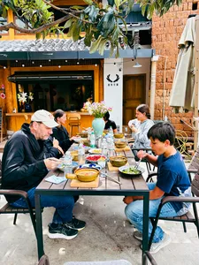 Group enjoying lunch outdoors in Lijiang at a brick courtyard table during a shared Yunnan cooking experience, with steaming bowls