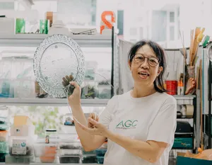 Tan Sock Fong holding a textured round glass piece at Art Glass Centre in Singapore, showing centrepiece skills—workshops in Singapore
