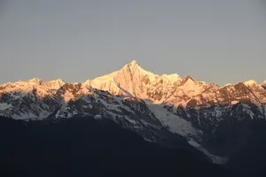 Snowy Meili Snow Mountain summit lit by early sunrise rays above dark ridgelines on a 2D2N adventure from Shangri-La