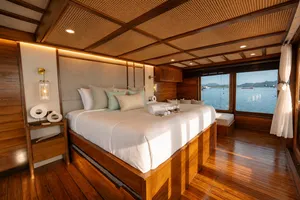 Wooden phinisi cabin with a made double bed, pillows, and seating by the window on a trip to Komodo Island