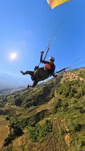 Tandem paragliding above grassy mountain ridges, with two orange-helmeted riders soaring against blue sky in Sapa