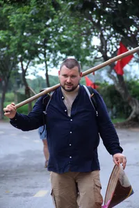 Doai Tour & Homestay host carrying a basket and hoe outdoors along a rural path during hands-on rice farming near Hanoi