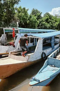 Traveller stepping off a wooden boat beside moored vessels, ready for a hidden mangroves and village visit in Labuan Bajo