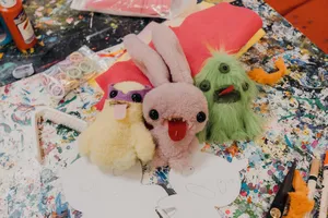 Ugly-cute plushie keychains in progress on a colourful craft table in Singapore, with felt pieces and scissors