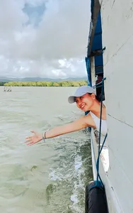 Smiling traveller holding onto a white boat rail as it moves through green seascapes during a hidden mangroves day trip, Labuan Bajo