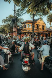 Suasana jalanan di Hoi An dalam tur Vespa berpemandu, para peserta berkumpul dengan skuter di luar toko dan kafe yang ramai