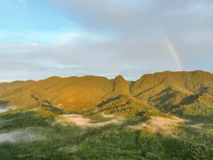 A rainbow arcs over green ridges and a winding river in the rainforest valley near Ngapuh Homestead, Kuching