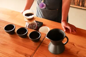 Coffee tasting table in Lijiang with black sample cups, a glass grinder jar, and a pour as visitors try Yunnan brews